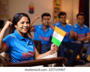 Bokeh shot of cricket fans watching a live match at home - a female fan holding an Indian flag in her hands, cheering up for team India. A group of friends huddled together- wearing a jersey - Powered by Shutterstock