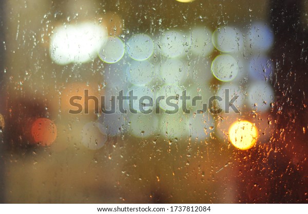 Bokeh through window in car in the raining\
night. Water drops on window.  Concept of autumn rainy weather.\
Abstract beautiful background and\
wallpaper