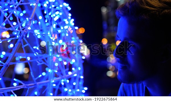 Bokeh view of a stylish young handsome man smoking\
electronic cigarette and breathing out smoke thru nose in city at\
night in summer