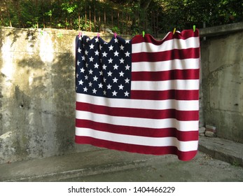 Bold American flag blanket hanging out to dry on a clothesline cornered by a bleak concrete wall
