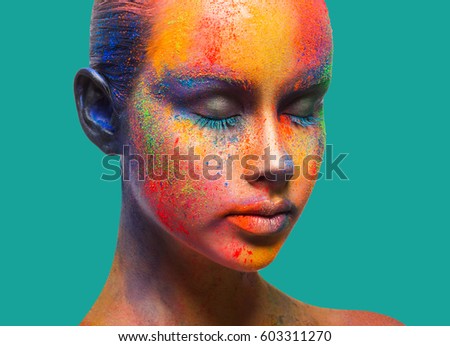 Bold color fantasy. Holi festival of colors background. Female face art with creative make up. Closeup studio portrait of young fashion model with eyes closed isolated on turquoise background