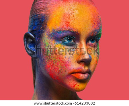 Bold color fantasy. Holi festival of colors background. Female face art with creative make up. Closeup studio portrait of young fashion model isolated on peach pink background