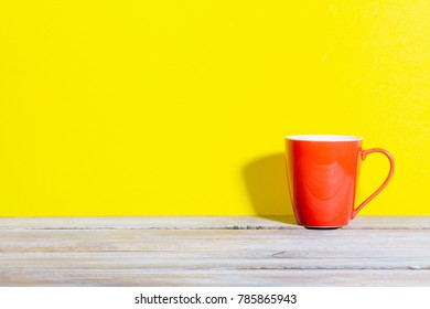 Bold Colored Red Coffee Mug On Wood Desk With Yellow Background And Shadow