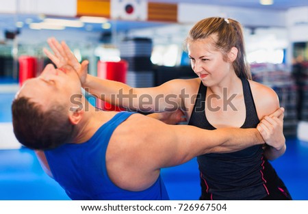 Bold positive  woman is training with man on the self-defense course in gym.