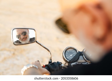 Bold Senior Man Looking At Rear-view Mirror While Riding Motorcycle On Summer Day