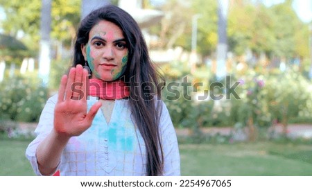 Bold urban girl showing stop sign with hands during Holi festival celebration. Indian lady covered with colorful Gulal asking to stop abuse violence against women on the occasion of Holi