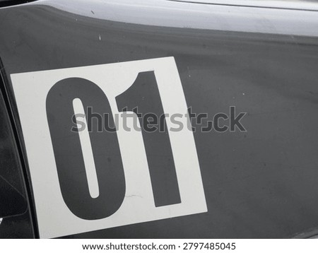 A bold white number zero one graphic decal sticker is applied onto a smooth dark black glossy metallic vehicle surface panel.