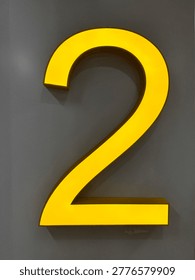 Bold yellow number 2 dimensional sign mounted on gray wall. Bright illuminated floor level indicator for modern interior.