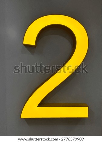 Bold yellow number 2 dimensional sign mounted on gray wall. Bright illuminated floor level indicator for modern interior.