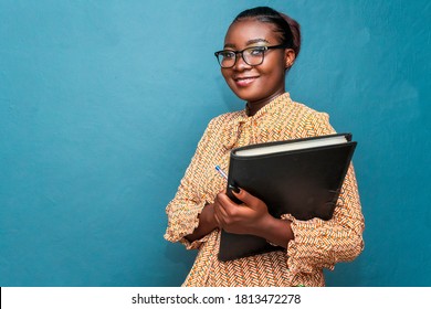 Bold,beautiful and confident African business woman or teacher holding a black file,isolated on blue studio background - Shutterstock ID 1813472278