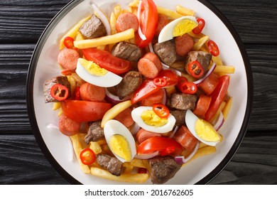 Bolivian Pique A Lo Macho is a dish prepared with cooked meat and sausage served over fries and garnished with vegetables, eggs closeup in the plate on the table. Horizontal top view from above