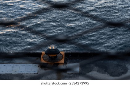 A bollard with "41" marked sits on a dock beside rippling water, viewed through a chain-link fence. - Powered by Shutterstock