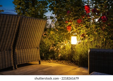 Bollard Light Hidden In Bushes Illuminating Cozy Patio In Landscaped Backyard Garden Of The Residential House. Outdoor Landscape Lighting Theme.