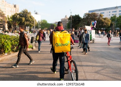 Bologna, Italy - 13 April 2019: Young Boy Glovo Rider Making Delivery On His Bike Working In The So Called Gig Economy Barcelona Main Square