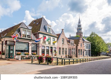 BOLSWARD, NETHERLANDS - AUG 20, 2017: Facades of historic houses and cafes on quay and tower of town hall in old town of Bolsward, Friesland