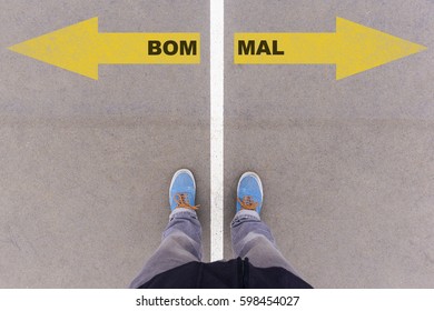 Bom E Mal, Portuguese Text For Good And Evil, Direction Sign Text On Asphalt Ground, Feet And Shoes On Floor, Personal Perspective Footsie Concept