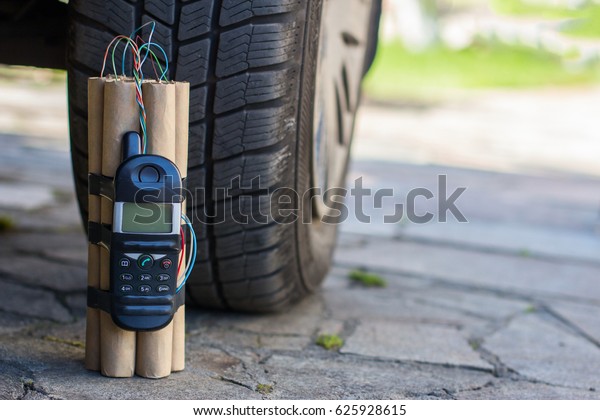 The bomb is under the car near the wheel tire. An\
explosive with a detonator mobile phone under the car. Terrorism.\
Empty place for text.