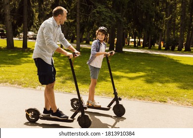 Bonding Concept. Father having ride on e-scooter with his cheerful son on the road in park, free space
