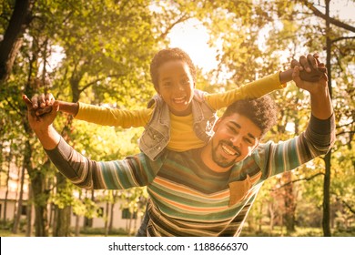 Bonding With Dad Smiling African American Father Carrying His Daughter On Piggyback And Holding Hands.