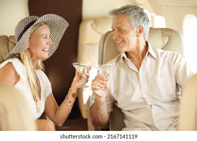 Bonding on a romantic getaway. Smiling and happy couple seated in a private jet and toasting each other.