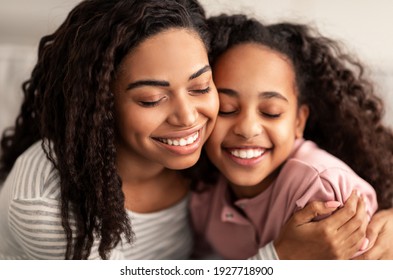 Bonding And Togetherness Concept. Close up portrait of African American mom and daughter hugging and smiling, celebrating mother's day, enjoying time together. Happy woman cuddling with girl