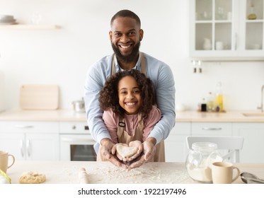 Bonding And Togetherness Concept. Portrait Of Happy African American Dad And Daughter Baking In The Kitchen And Holding Dough In Heart Shape In Hands, Preparing Present For Mother's Day
