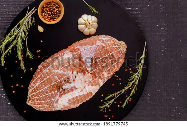 Boneless pork shoulder with spices on black wooden\
board. Holiday food.
