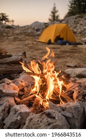 Bonfire burning in tourist camp in mountains. Beautiful campfire, burning wood by tent in summer evening. Active lifestyle, traveling, hiking and camping concept. Campfire burning in slow motion
