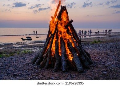 A Bonfire On The Shore Of The Baltic Sea. People At Sunset By The Sea, Riga Gulf.