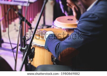 Bongo drummer percussionist performing on a stage with conga drums set kit during jazz rock show performance, with latin cuban band performing in the background, drummer point of view 