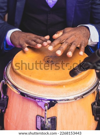 Bongo drummer percussionist performing on a stage with conga drums set kit during jazz rock show performance, tumbadora quinto with latin cuban afro-cuban jazz band performing in the background