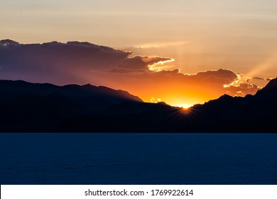 Bonneville Salt Flats Dark Blue Landscape Near Salt Lake City, Utah And Silhouette Mountain View And Sunset Sun Rays Glowing Behind Clouds