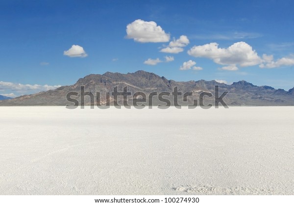  Bonneville Salt Flats in early morning. Mountains\
in center and a bright blue sky above with several puffy white\
clouds./ Classic Bonneville Salt Flats View / Lots of beauty and\
and but very harsh.
