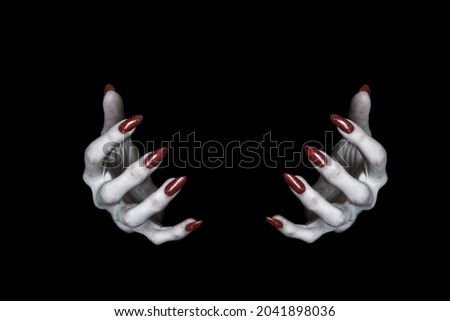 Bony pale hands of vampire or monster with sharp bloody red nails in the dark. Witch fingers hold something, low key, selected focus.