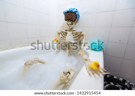 Bony skeleton taking a bubble bath in a grungy off-white dirty tub