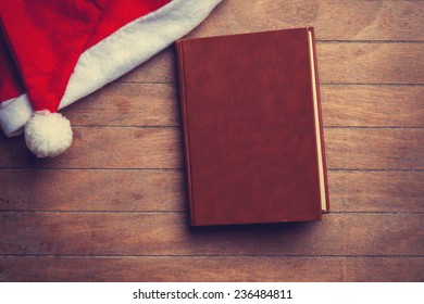 Book And Christmas Hat On Wooden Table.