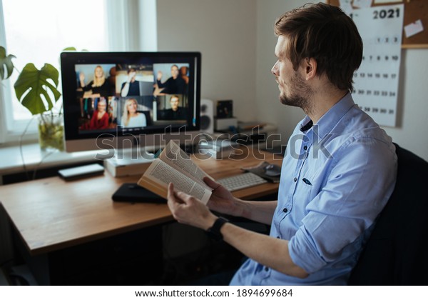 Book Club Online. Handsome young man in casual clothes\
reading a book in a video conference call  Boring group video chat \
While Practicing Social Distancing. Online education video\
conferencing 