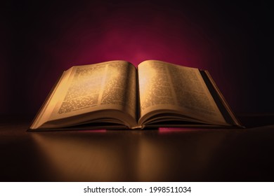 Book emitting light on a dark background. An open book is reflected in table. Book as a symbol of bible. Concept - reading christian literature. Open bible with text close-up. Bible with blurry text - Shutterstock ID 1998511034