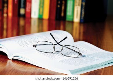 Book With Glasses On The Desk Against Books