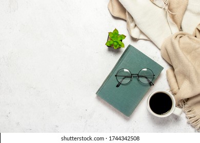 Book, glasses with round glasses, a woolen plaid, a cup with coffee and a flower indoor on a light background. Leisure concept, reading a book. Flat lay, top view - Powered by Shutterstock