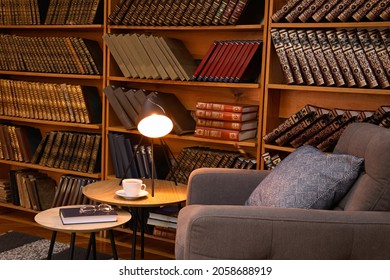 Book With Glasses, Table Lamp And Cup Of Drink Near Comfortable Armchair In Cozy Home Library