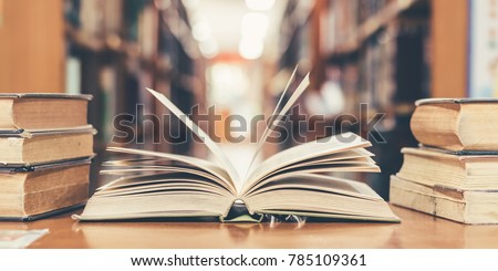 Book in library with old open textbook, stack piles of literature text archive on reading desk, and aisle of bookshelves in school study class room background for academic education learning concept