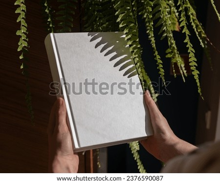 Book mockup and green plant. Hard cover, clean clear empty blank hardcover in hands