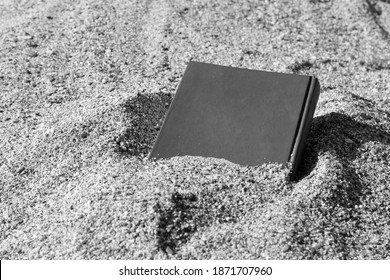 Book on the sand on a blurry background, covered with sand, buried in the sand, monochrome
