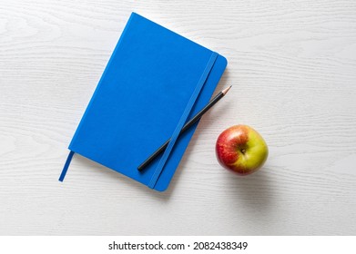 Book on table, blue hardcover with an apple and pencil