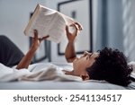 Book, reading and relax with teen on bed in home for weekend education, literature or study. Hobby, novel or storytelling with boy in bedroom of apartment for development, growth or learning