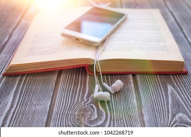 book, smartphone, headphones on a wooden background. audiobook. hobby. free time. recreation. literature.