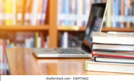 Book Stack And Laptop Computer On Workplace In Library Room With Blurred Bookshelf Background, Education Concept 