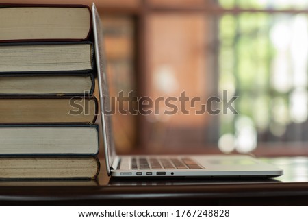 book stack and laptop on desk in library. e-book digital technology and e-learning class concept.