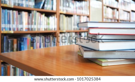 Book stack on wood desk and blurred bookshelf in the library room, education background, back to school concept